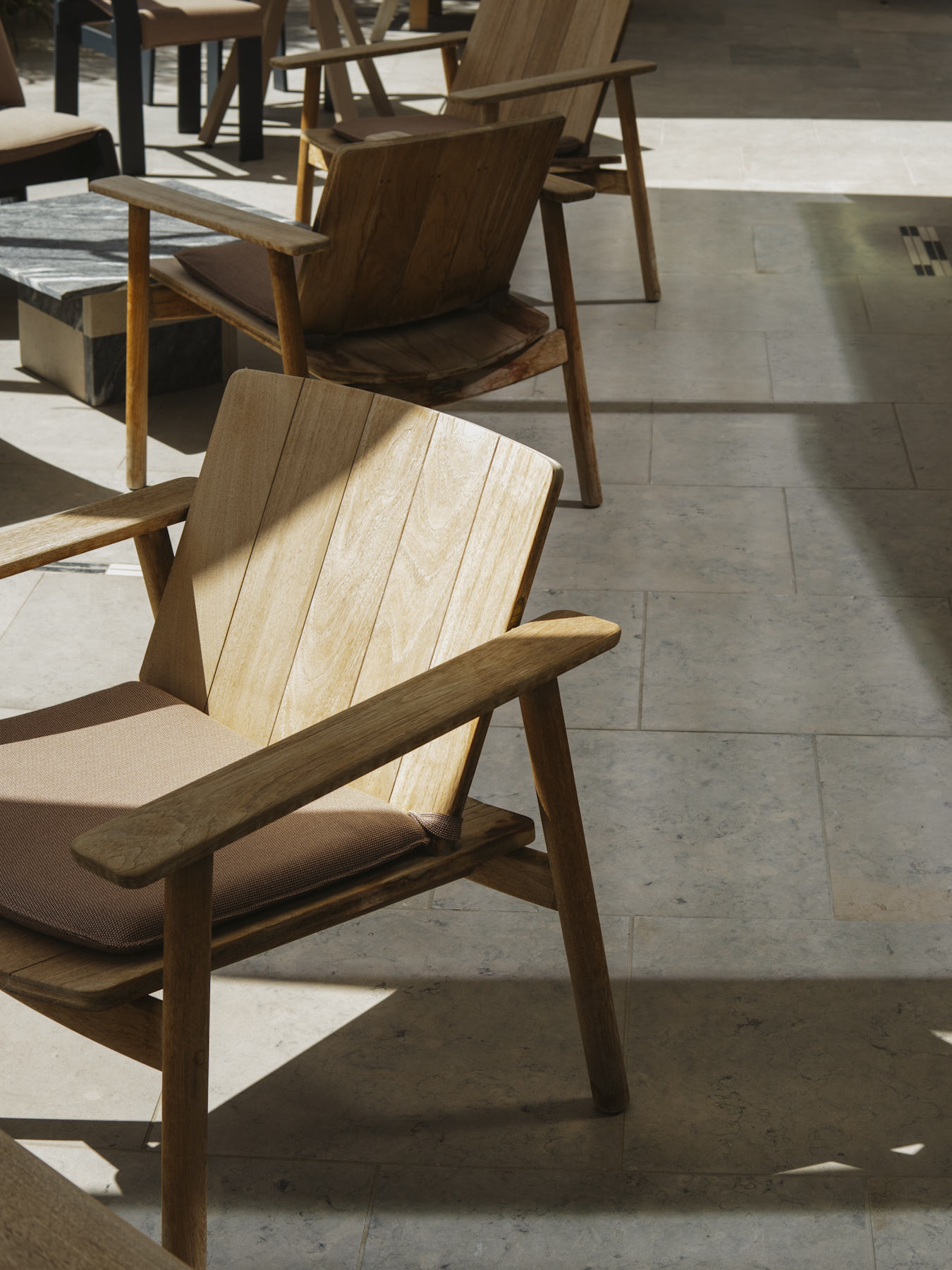 Teak lounge chairs on a limestone terrace in dappled light