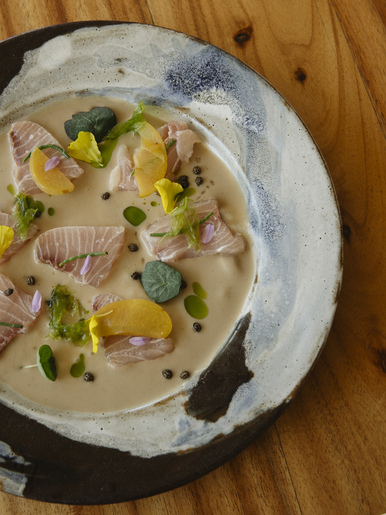 Slices of raw fish in a pale broth with nasturtium leaves, capers and edible flowers