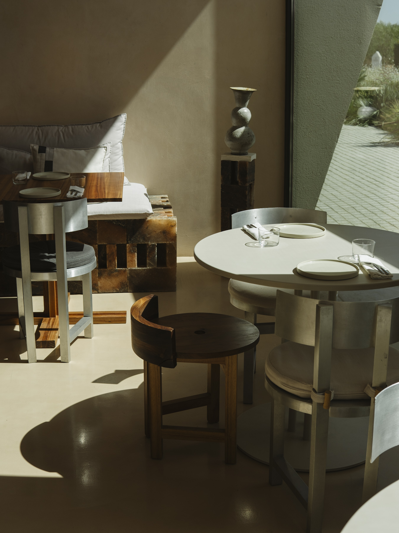 Round table and curved metal chairs beside a full-height window at Austa