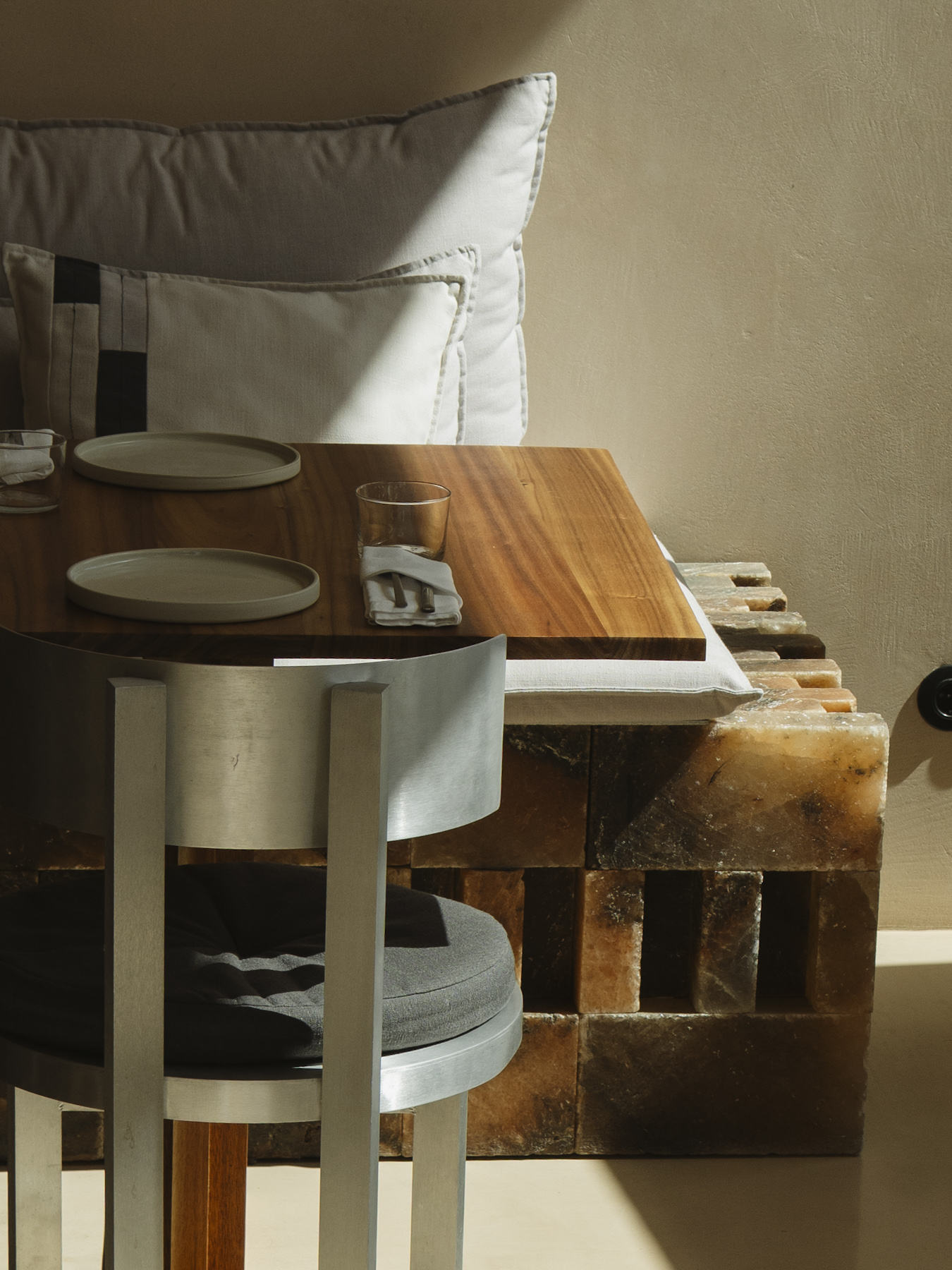 A solid timber table set with plates and a napkin against a rough stone bench