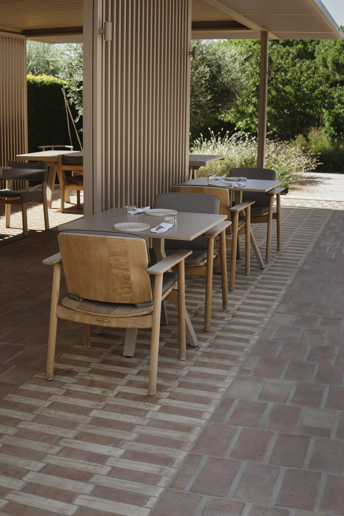 A row of laid tables and wooden chairs on a herringbone brick terrace
