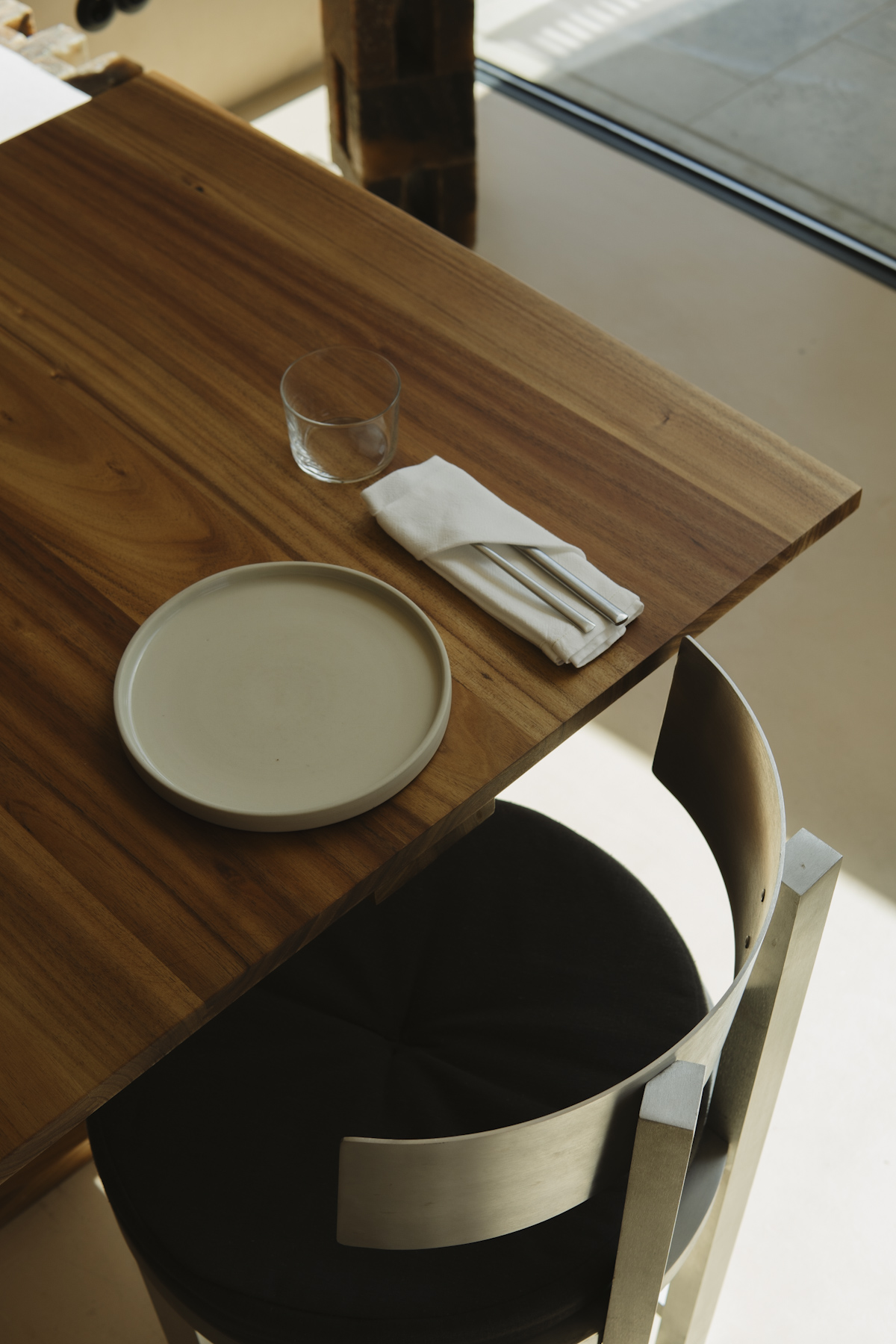 A single plate, glass and folded napkin on the corner of a timber table