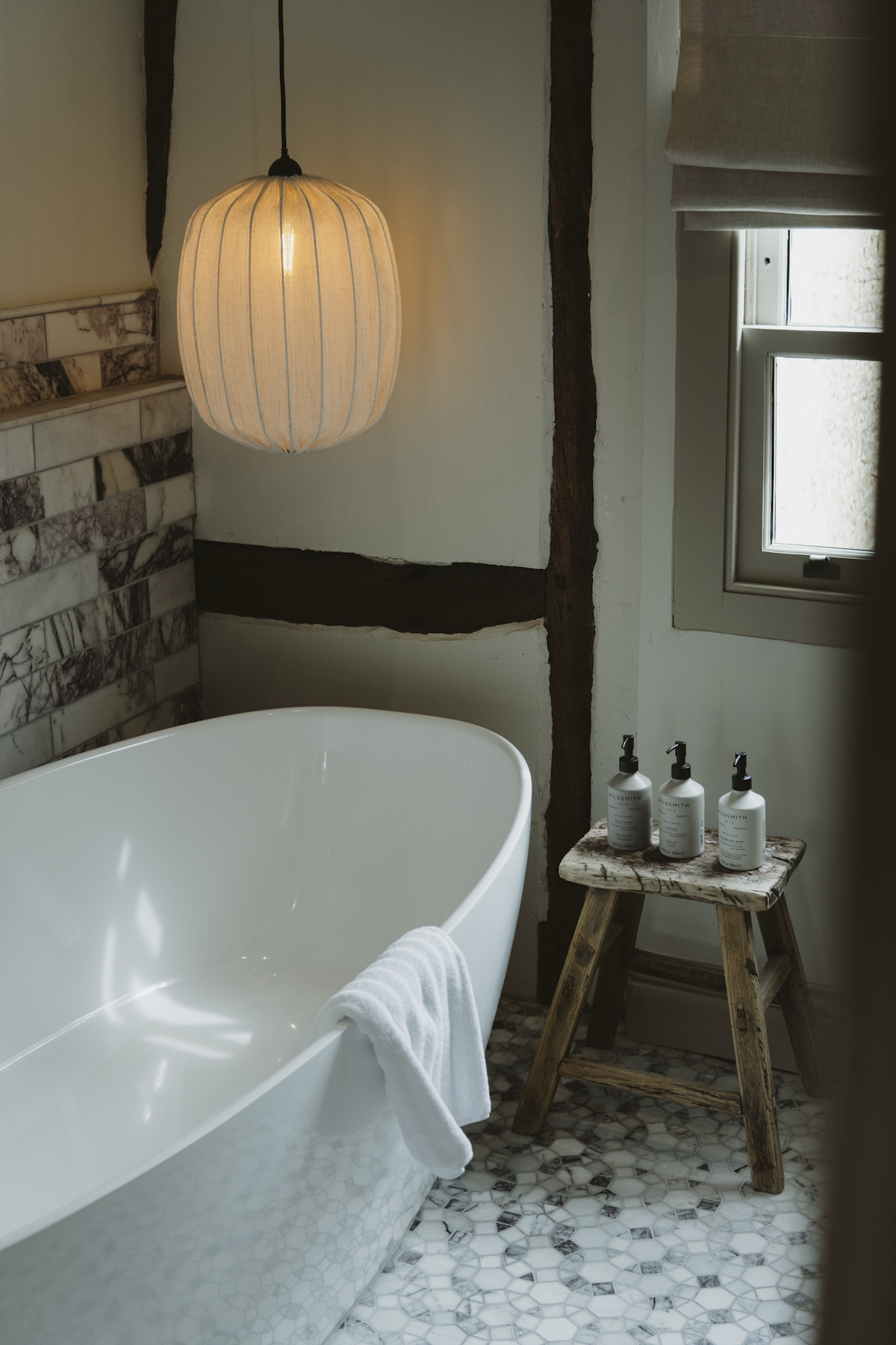 A freestanding bath beside a timber beam, with toiletries on a rustic stool