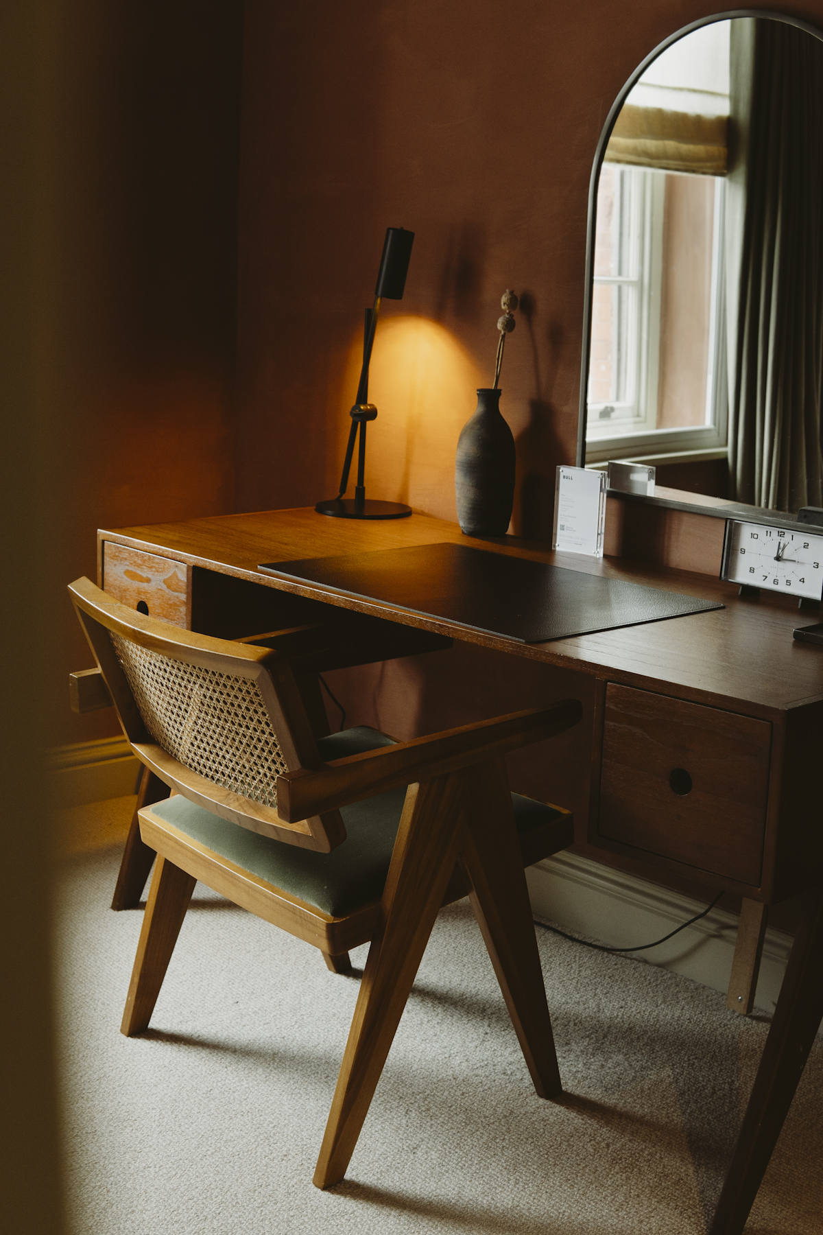 A writing desk and cane chair under an arched mirror in a suite