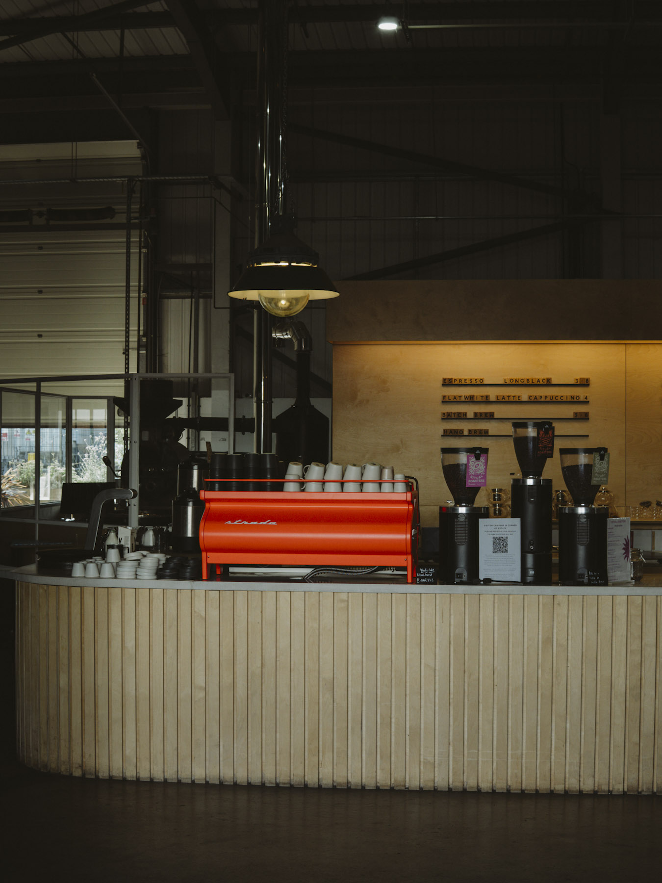 Red espresso machine on a fluted counter under a pendant light